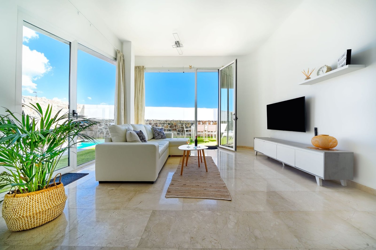 Living room with large television, lounge furniture and views of the pool and garden - Villa Estación 1 - Salobre Resort